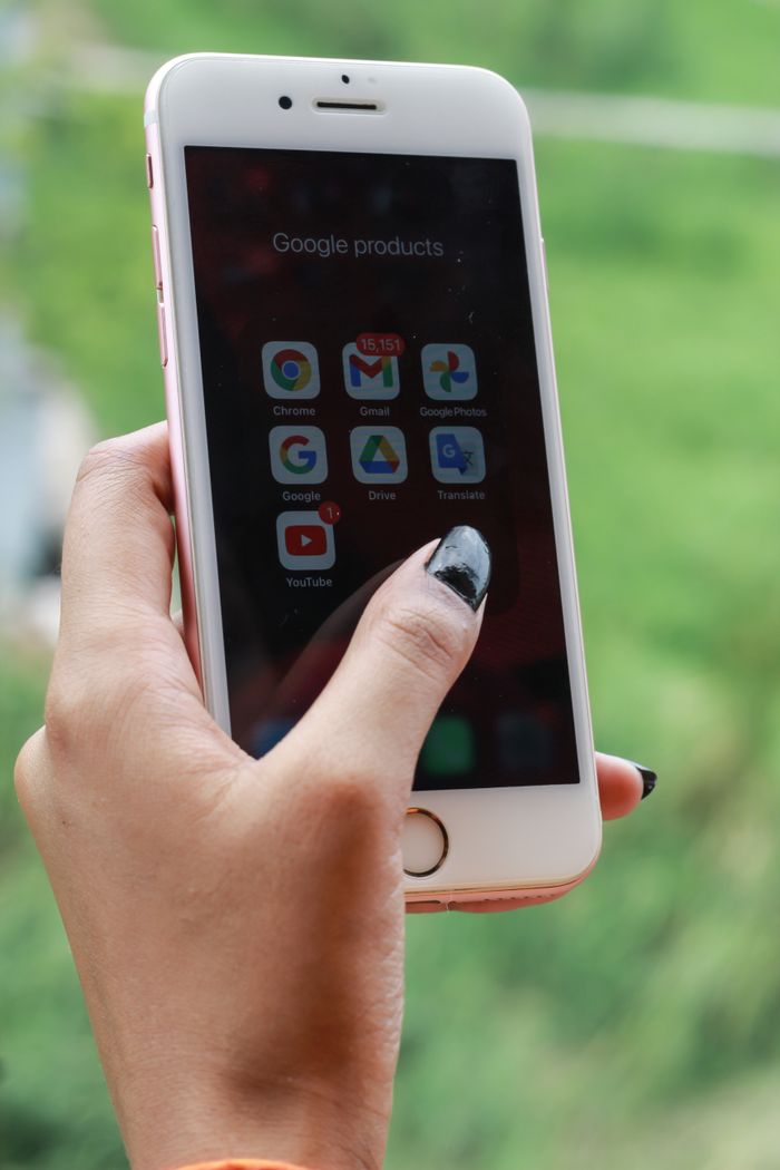 our-mission Hand with black nails holding a smartphone showing Google apps outdoors.